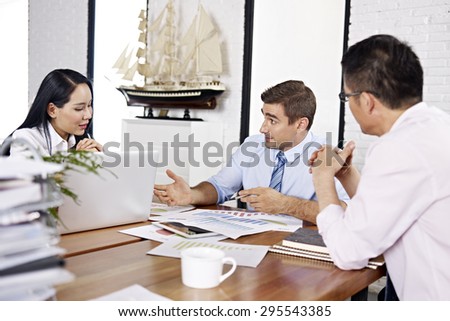 asian and caucasian business executives reviewing and discussing business performance in office of a multinational company.