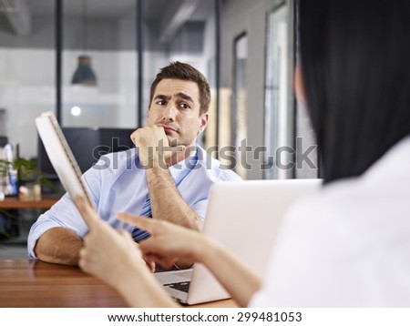 a caucasian male interviewer looking skeptical while listening to an asian female interviewee.