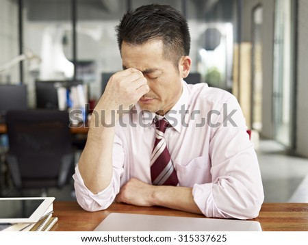 asian businessman looking tired and frustrated in office.