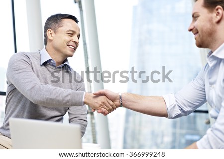 two caucasian businesspeople smiling and shaking hands in office.