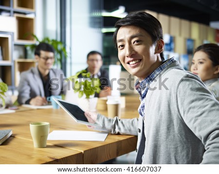 young confident asian businessman turning to look at camera during meeting in office.
