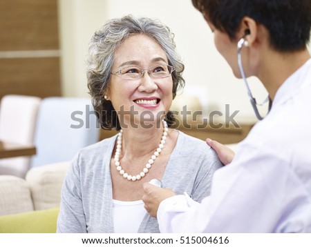 family doctor checking smiling senior asian woman using stethoscope