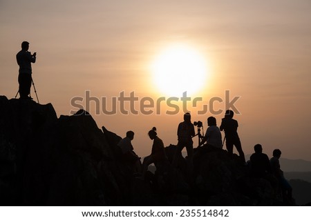 Stylish silhouette image of many photographers on the rocky hills. At the time when the sun is below the horizon.