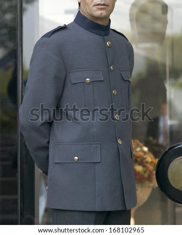 Bellhop with grey uniform opening door of a Hotel building
