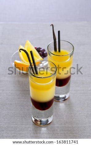 layered cocktail in a glass with orange and currants, with straw and stick vanilla