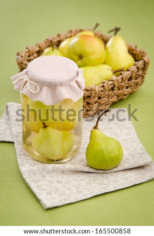 Home preservation canned pear compote in jar with a basket of fruit and in the background