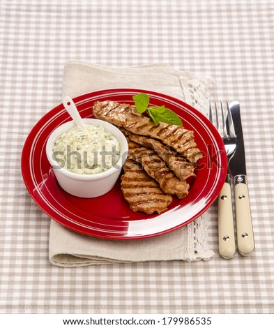 juicy grilled meat with white sauce on a red plate