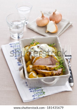 Baked pork meat with potatoes with white sauce and thyme in a ceramic dish