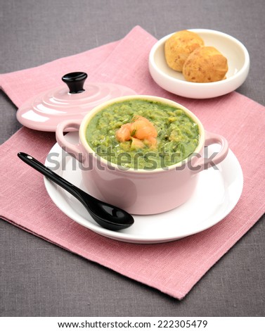 green vegetable puree soup with salmon in a pink ceramic bowl with bread rolls in the background