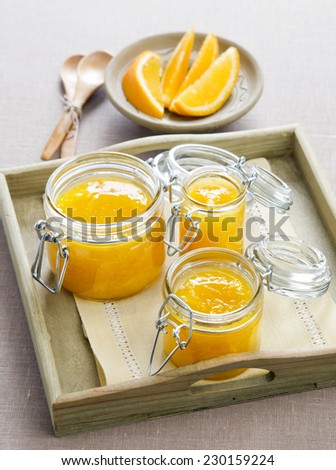 orange marmalade in glass jar on a wooden tray with slices of orange in the background
