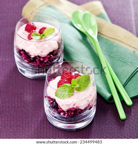 Oatmeal with raspberries currants yogurt in a glass cup with mint on a purple background with green spoons