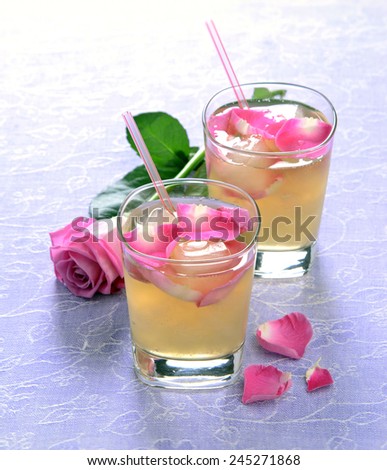 Cocktail with rose petals in a glass with a straw with a rose in the background
