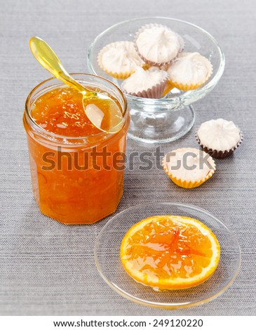 orange jam with candied fruit in a glass jar with marshmallows in the background