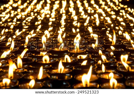 Lighted candles lined up in a row and glow in the dark space. Monastery in Nepal. Tibet, the Himalayas.
