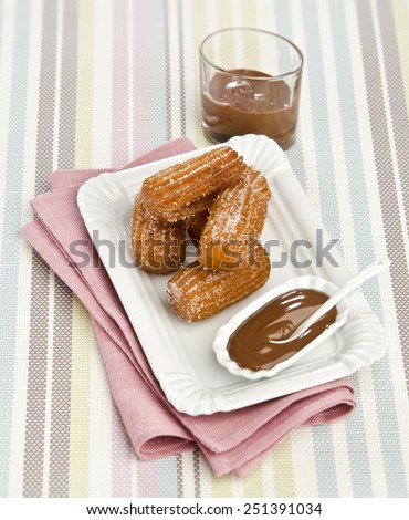 Churros with chocolate sauce on a white plate striped background in pastel colors