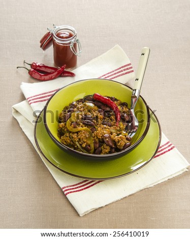 Mexican chili beans with ketchup pepper in green plate on a napkin linen with ketchup in the background