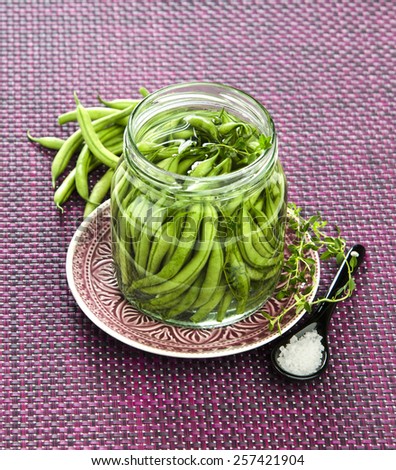 Canned green beans with salt in a glass jar on a purple background