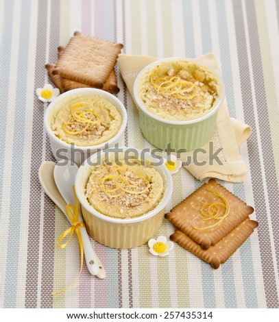 small ramekiny with baked lemon cream decorated with biscuits and sweet flowers on striped background