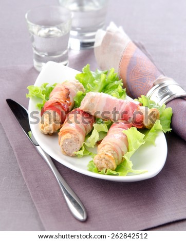 white Bavarian sausages wrapped in bacon on a white plate with lettuce cups in the background