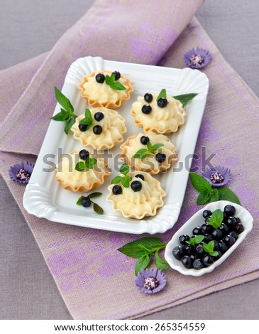 dessert mini tartlets with cream and blueberries with mint leaves in a white plate on a purple background
