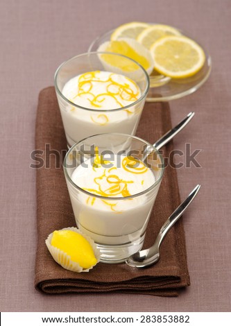 lemon mousse in glass cups dusted lemon peel on a brown napkin with a dessert spoon next to a dark beige background