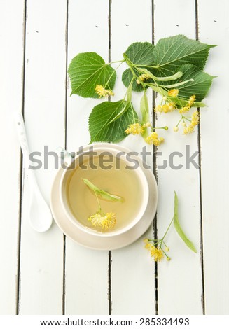 linden tea in a porcelain cup with blossoming linden branch in the background on a white wooden table