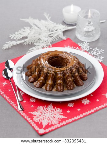 Christmas pudding poured with caramel chocolate on a table decorated for Christmas with candles in the background a red napkin with snowflakes