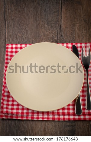 Empty plate with fork and knife on tablecloth over wooden background, closeup