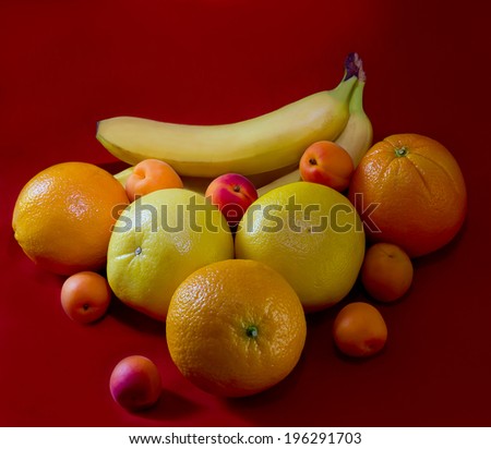 Oranges,bananas,yellow grapefruit and delicious apricots on a red background