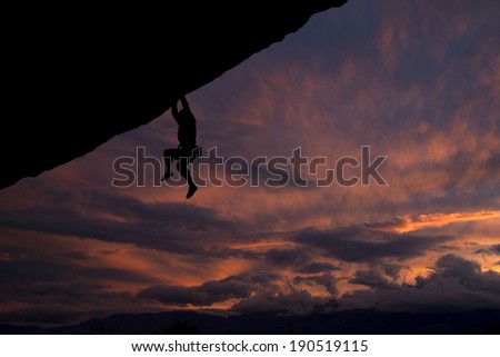 Rock climber hanging off overhanging cliff with a nice sunset background