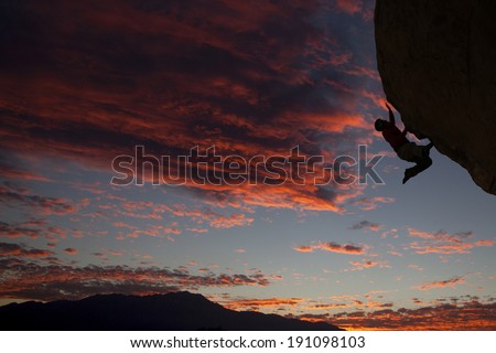 Rock climber climbing an overhanging cliff with a nice sunset