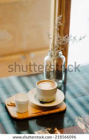 A cup of latte coffee with cracker in warm tone light coffee cafe\'