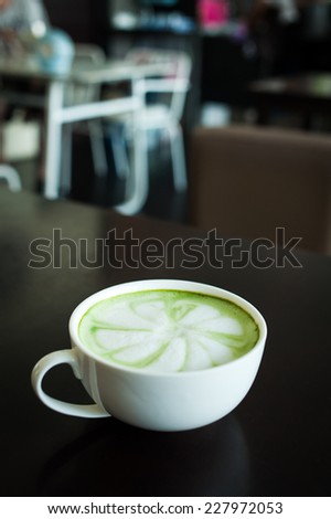 Hot milk green tea (selective focus) in the white cup on the dark wooden table.