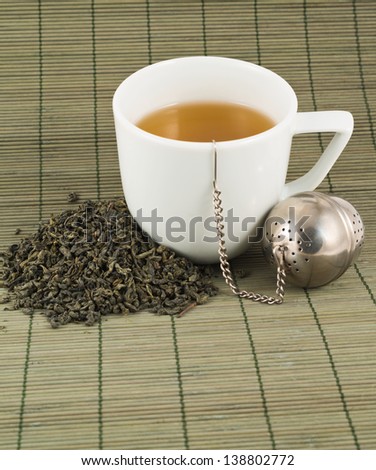 White cup of green tea with the heap of tea over bamboo mat