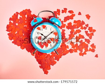 Alarm clock over the heart shape made of red confetti