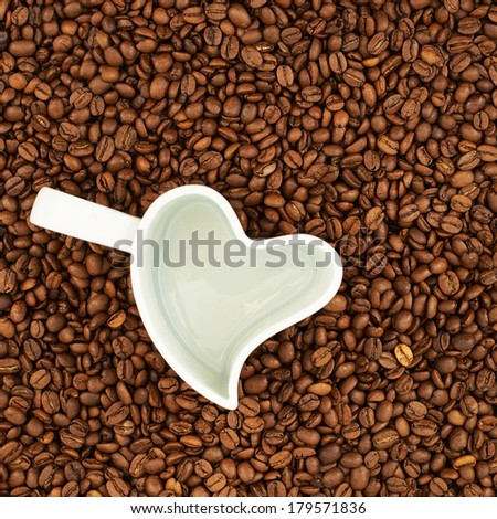Empty heart shaped coffee cup over the surface covered with coffee beans