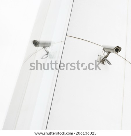 One CCTV camera installed to the wall next to its own reflection in the glass