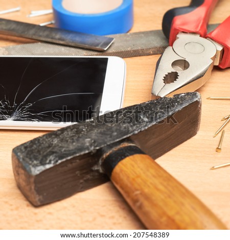 Repair mobile phone composition of a smartphone with a broken screen next to the multiple tools over a wooden surface