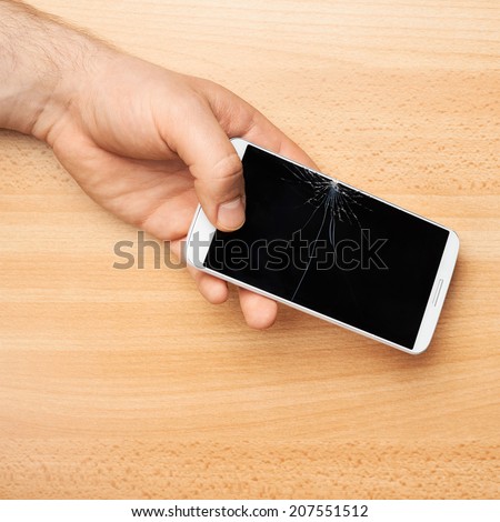 Hands holding a mobile phone with a broken screen over the wooden surface