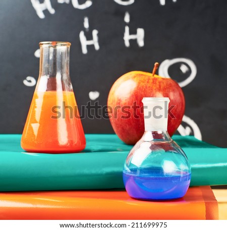 Chemistry glass tubes and vessels filled with liquids over the stack of colorful books against the blackboard composition