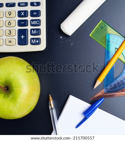 Studying back to school composition of the green apple and some stationery office supplies over the black background