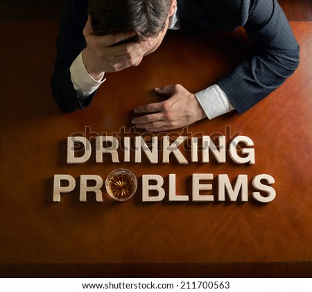 Phrase Drinking Problems made of wooden block letters and devastated caucasian man in a black suit sitting at the table with the glass of whiskey, top view composition with dramatic lighting