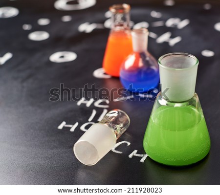 Chemistry glass tubes and vessels filled with colorful liquids over the blackboard\'s surface with some chemistry structures drawn with chalk, shallow depth of field composition