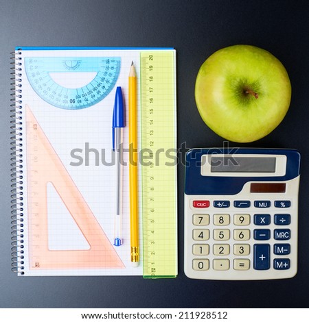 Studying back to school composition of the green aplle and some stationery office supplies over the black background
