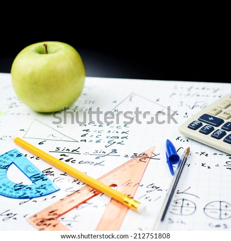 Studying math back to school composition of the green apple and some stationery office supplies lying over the sheet filled with trigonometry equations and formulas