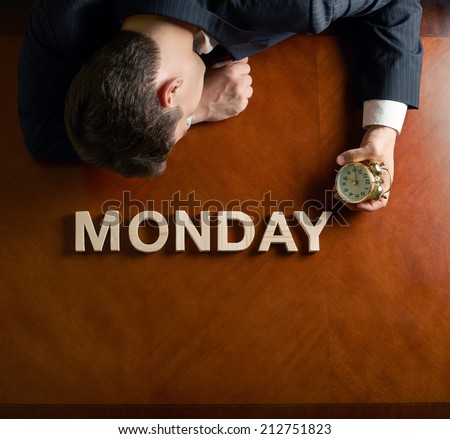 Word Monday made of wooden block letters and devastated middle aged caucasian man in a black suit sitting at the table, top view composition with dramatic lighting