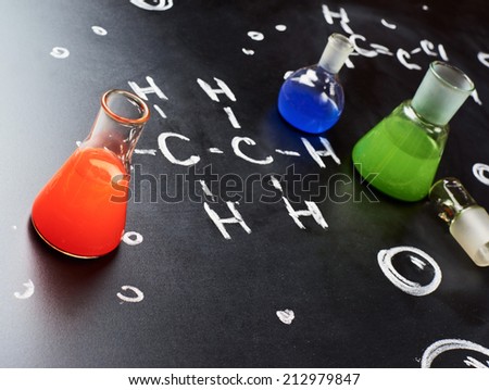 Chemistry glass tubes and vessels filled with colorful liquids over the blackboard\'s surface with some chemistry structures drawn with chalk