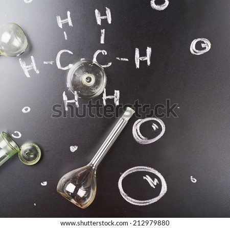 Multiple glass tubes and vessels over the blackboard with some chemistry structure formulas written over it