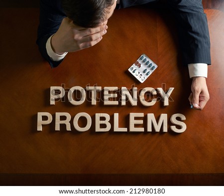 Phrase Potency Problems made of wooden block letters and devastated middle aged caucasian man in a black suit sitting at the table, top view composition with dramatic lighting