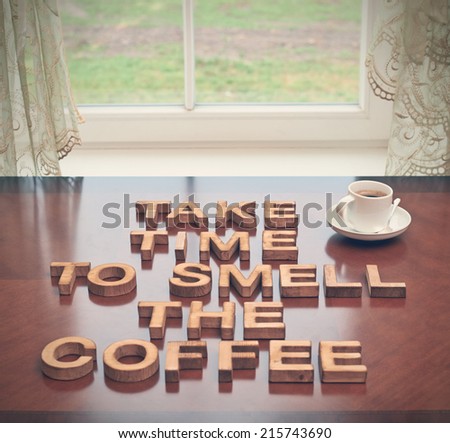 Take time to smell coffee quote made with the block wooden letters over the table, next to a cup of coffee, composition with tone image correction